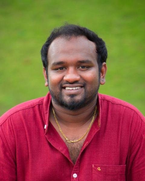 Vishnu Vijay smiling in a maroon shirt and gold chain against a green lawn, head-and-shoulders portrait