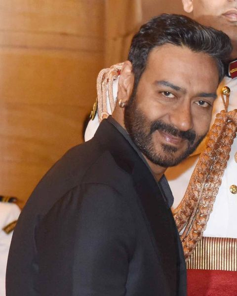 Ajay Devgn in a dark suit at a formal event with a ceremonial guard