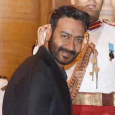 Ajay Devgn in a dark suit at a formal event with a ceremonial guard