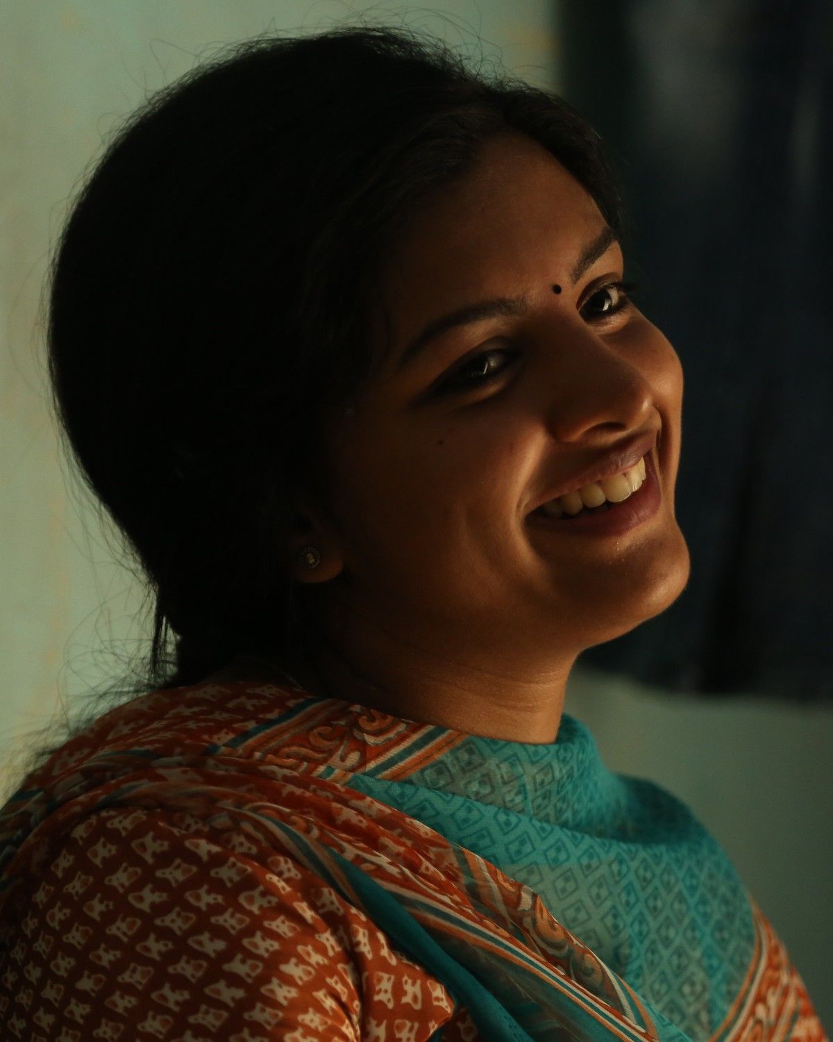 Lijomol Jose smiling in a dimly lit room, close-up portrait