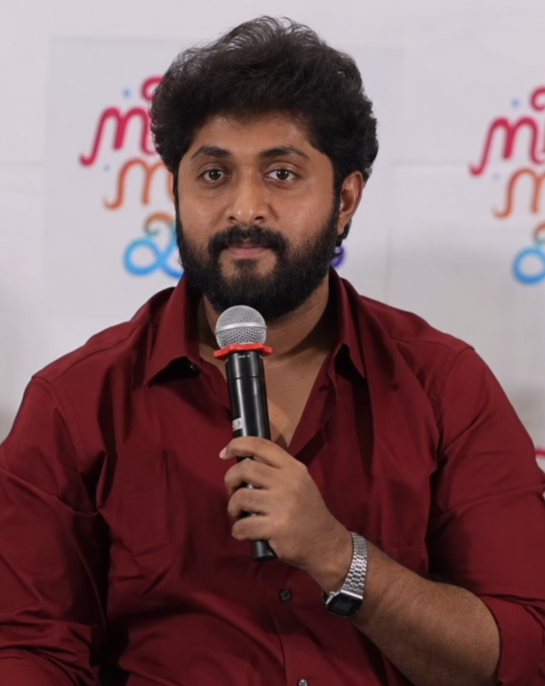 Dhyan Sreenivasan speaking into a microphone in a red shirt