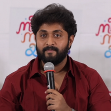 Dhyan Sreenivasan speaking into a microphone in a red shirt