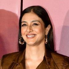 Tabu smiling in a brown blazer, close-up portrait