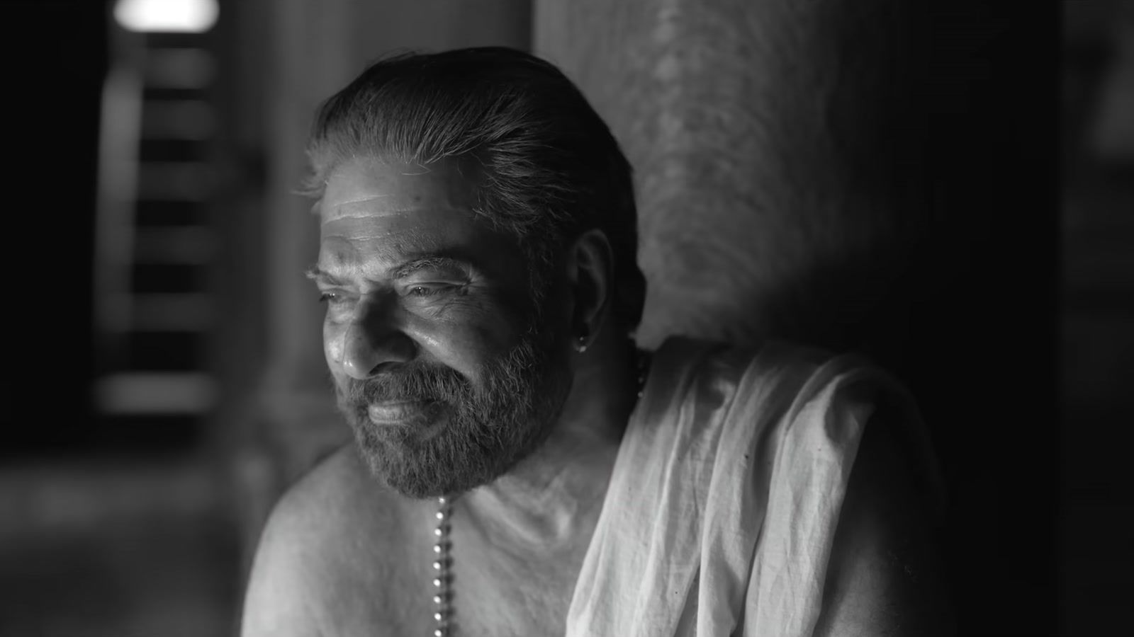 Mammootty smiling in a white mundu in a black-and-white frame from the Bramayugam trailer