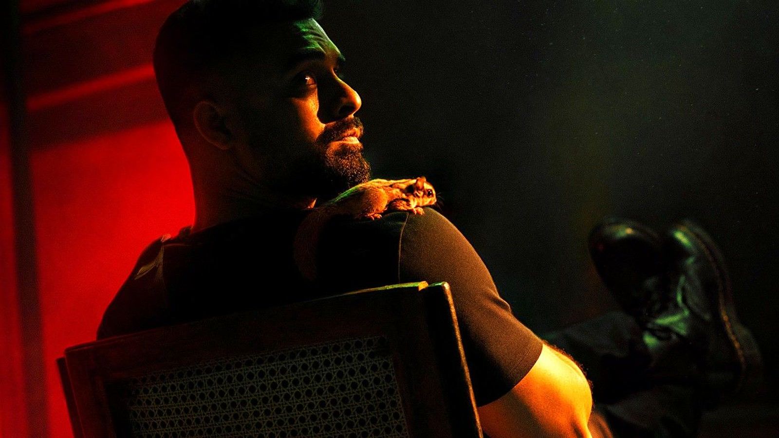 Tovino Thomas with a sugar glider on his shoulder, lit in red, in a Bachelor Party D'eux poster