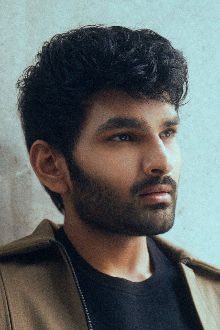 Aniesh Reddy with dark wavy hair and stubble in a jacket, portrait