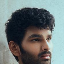 Aniesh Reddy with dark wavy hair and stubble in a jacket, portrait