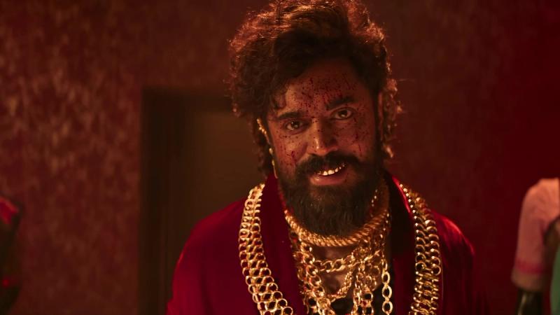 Nivin Pauly as Walter, bearded and wearing heavy gold chains and a red robe, in a red-lit room in the official Benz promo
