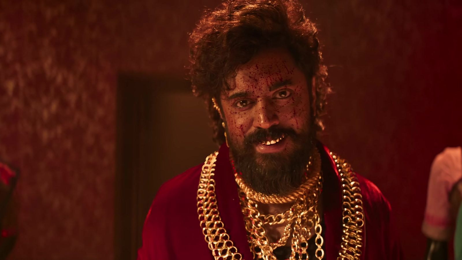 Nivin Pauly as Walter, bearded and wearing heavy gold chains and a red robe, in a red-lit room in the official Benz promo