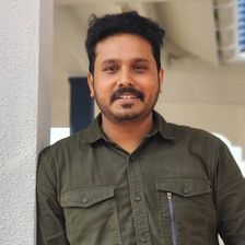 Nahas Hidhayath in an olive shirt, smiling, leaning against a white pillar