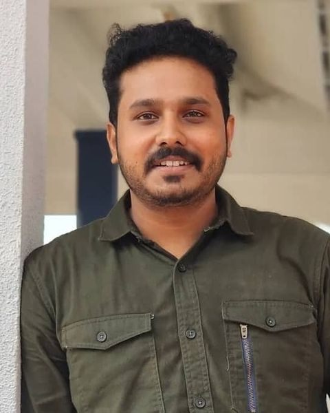 Nahas Hidhayath in an olive shirt, smiling, leaning against a white pillar
