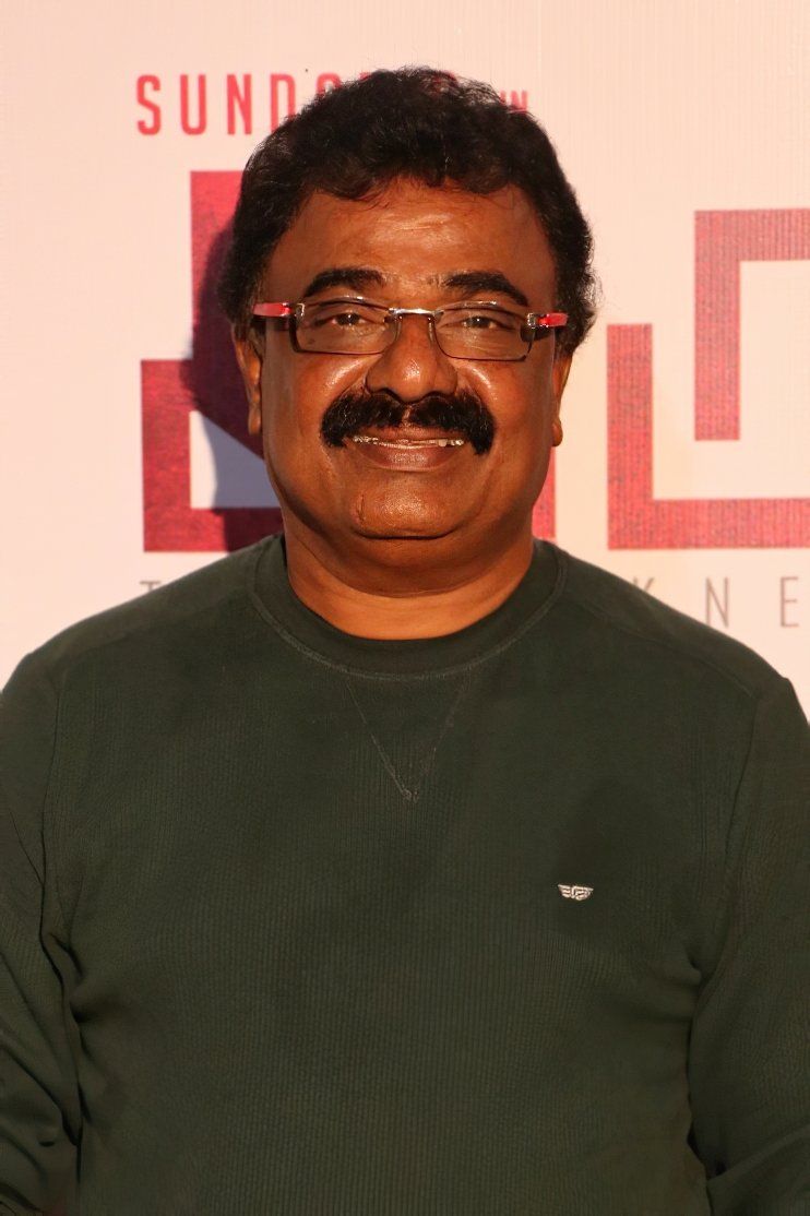 VTV Ganesh in rimless glasses and a dark green sweater at an event backdrop