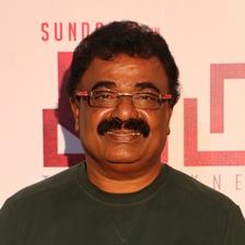 VTV Ganesh in rimless glasses and a dark green sweater at an event backdrop