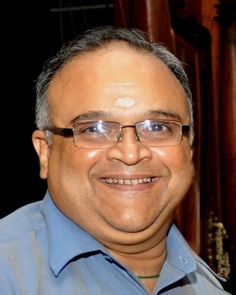 Mohan Raman smiling in glasses and a blue shirt, portrait