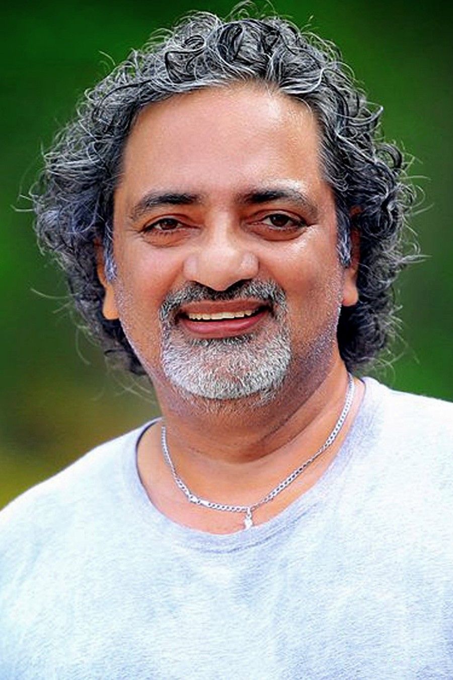 Joy Mathew with grey curly hair and a white beard in a white T-shirt, smiling