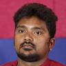 Bala Saravanan in a red shirt against a red and blue backdrop, head-and-shoulders portrait