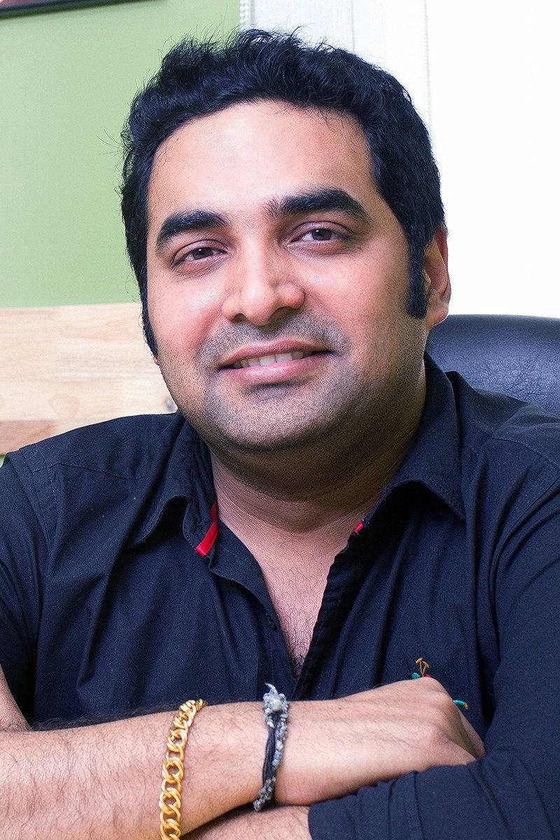 Gopi Sundar smiling in a dark shirt, seated indoors portrait