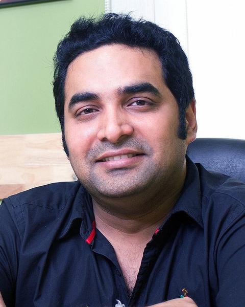 Gopi Sundar smiling in a dark shirt, seated indoors portrait