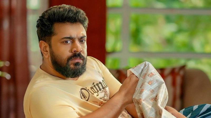 Nivin Pauly with a beard, seated on a sofa holding a newspaper, in the NP 51 birthday poster