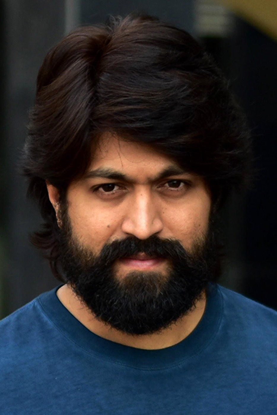 Yash with long hair and a full beard in a blue shirt, close-up portrait