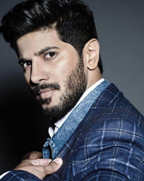 Dulquer Salmaan in a checked blazer against a dark background, portrait