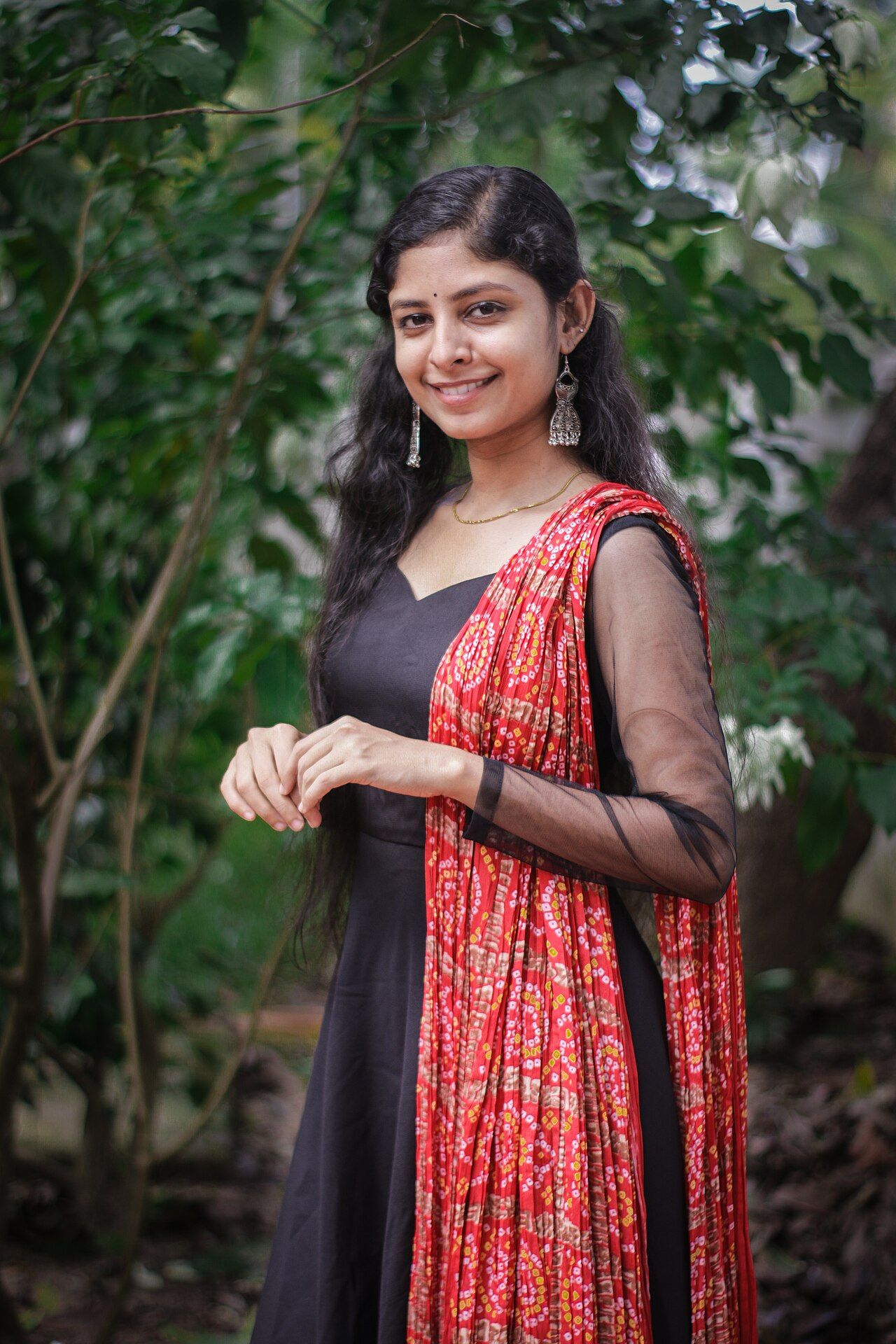 Akhila Bhargavan in a black and red outfit standing among green trees