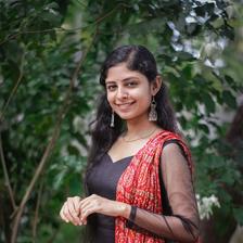 Akhila Bhargavan in a black and red outfit standing among green trees