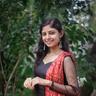 Akhila Bhargavan in a black and red outfit standing among green trees
