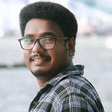 Aneesh Gopal in glasses and a checked shirt by a waterfront