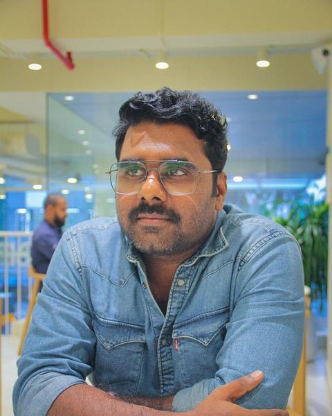 Sajin Cherukayil in glasses and a denim shirt, seated at a table