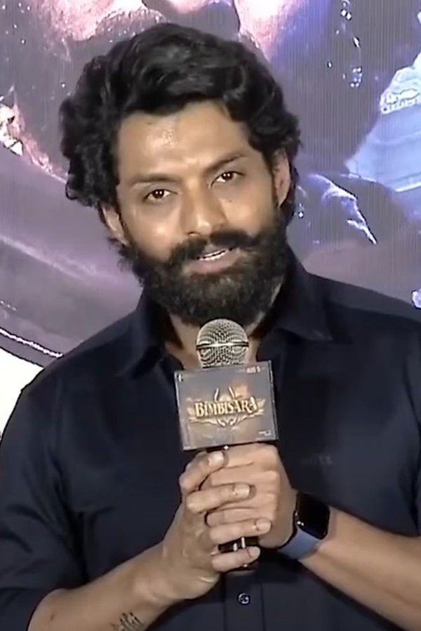 Nandamuri Kalyan Ram with a beard in a black shirt, speaking into a microphone at a press event