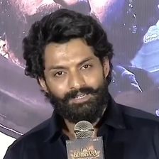 Nandamuri Kalyan Ram with a beard in a black shirt, speaking into a microphone at a press event