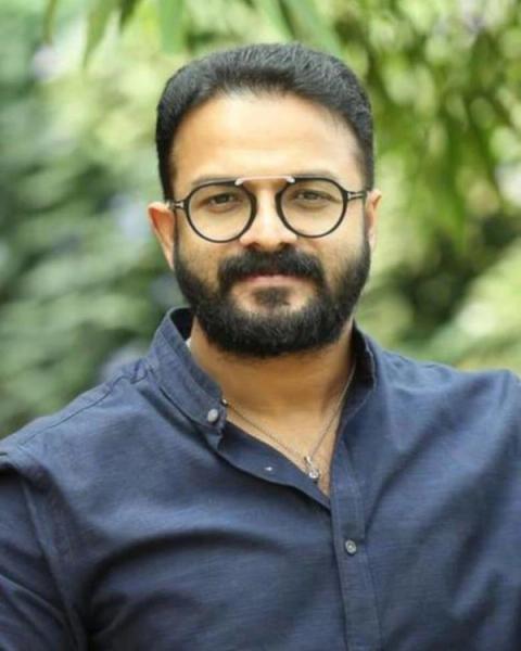 Jayasurya in round glasses and a blue shirt outdoors, portrait