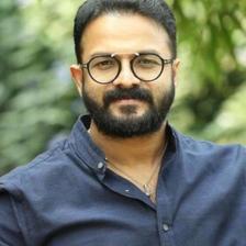 Jayasurya in round glasses and a blue shirt outdoors, portrait