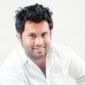 Aju Varghese smiling in a white shirt against a plain background