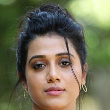 Shilpa Manjunath with her hair tied up, wearing a black top and layered necklaces against green foliage, portrait