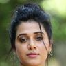 Shilpa Manjunath with her hair tied up, wearing a black top and layered necklaces against green foliage, portrait