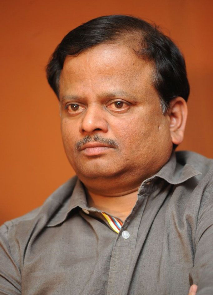 K. V. Anand in a grey shirt against an orange background