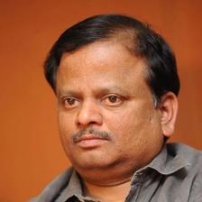 K. V. Anand in a grey shirt against an orange background