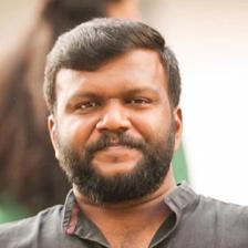 Manu Ashokan with a beard in a grey shirt, close-up portrait