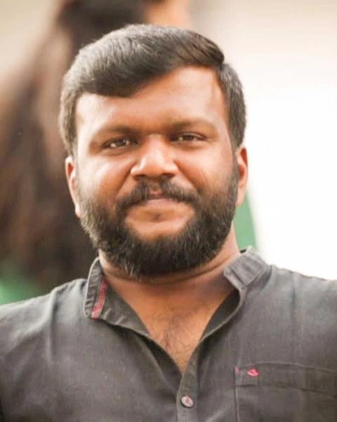 Manu Ashokan with a beard in a grey shirt, close-up portrait