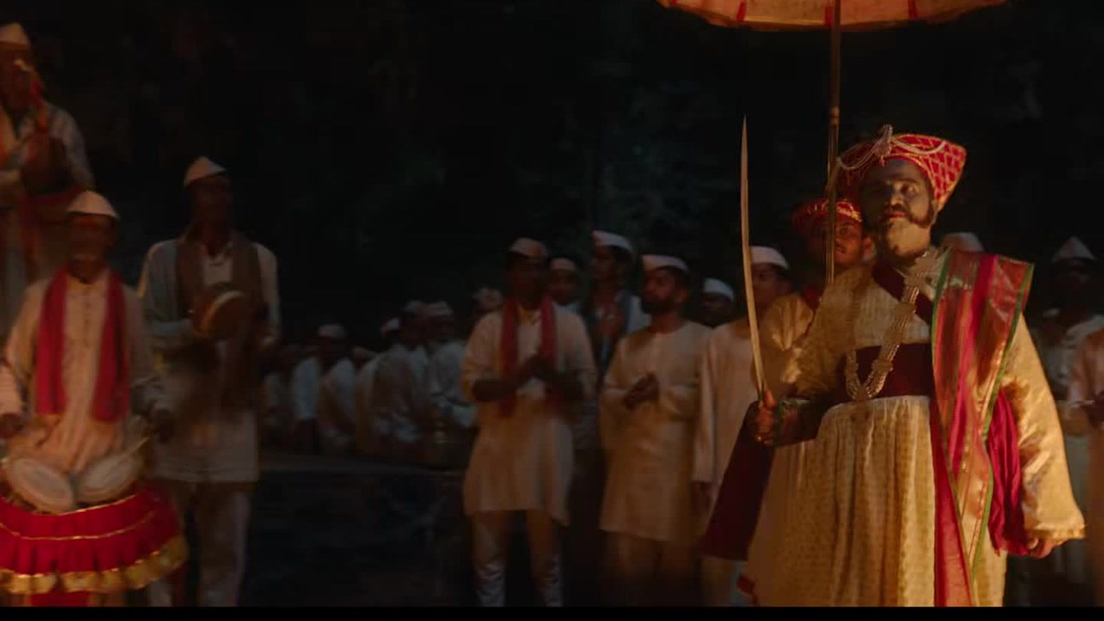 A folk procession under a ceremonial umbrella in a frame from the Gondhal trailer