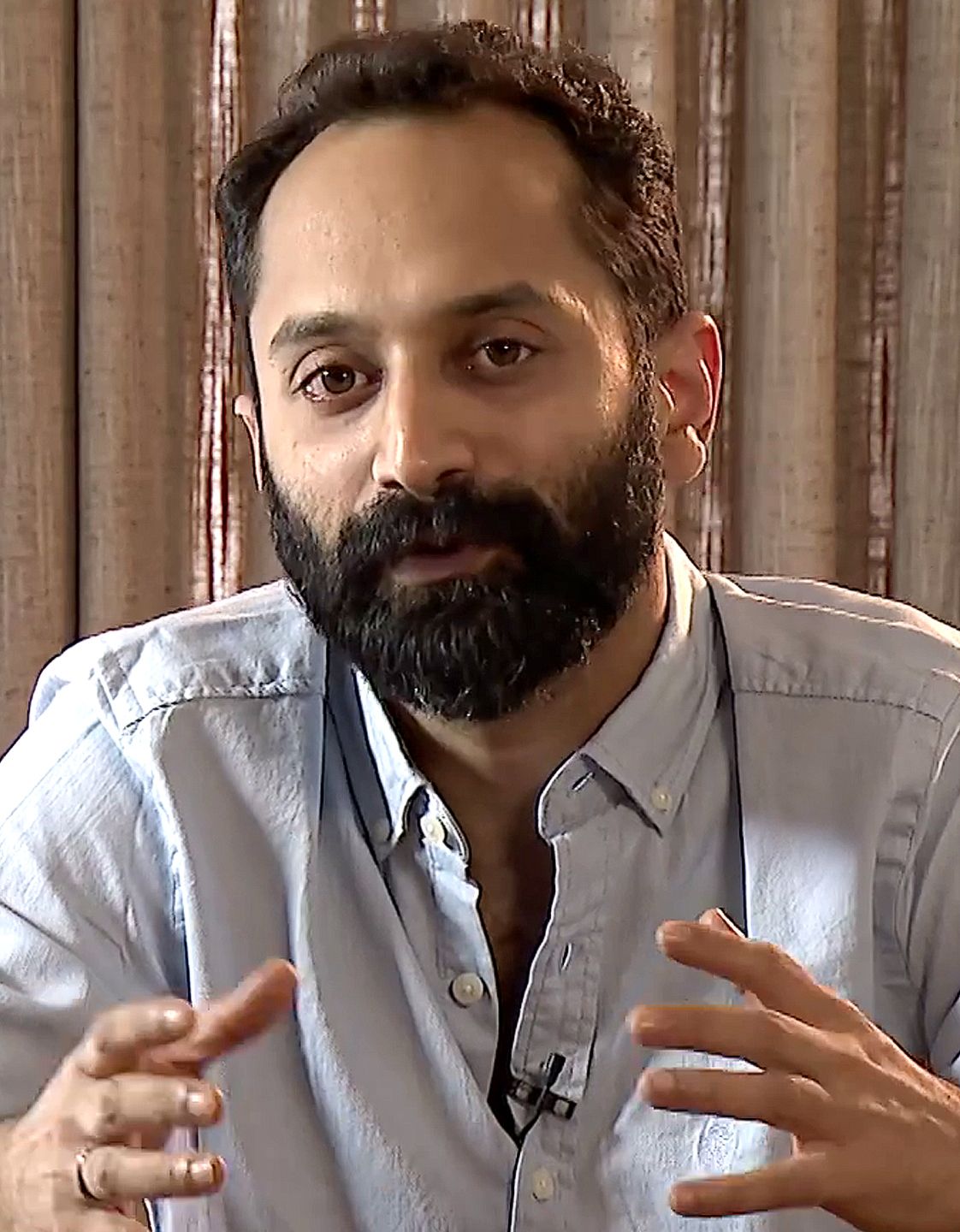 Fahadh Faasil with a beard in a grey shirt, gesturing while talking