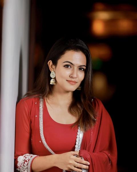 Aparna Das in a red outfit with a white dupatta, leaning against a pillar