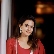 Aparna Das in a red outfit with a white dupatta, leaning against a pillar
