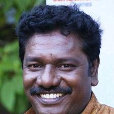 Karunas smiling widely with a moustache and gold chain, close-up
