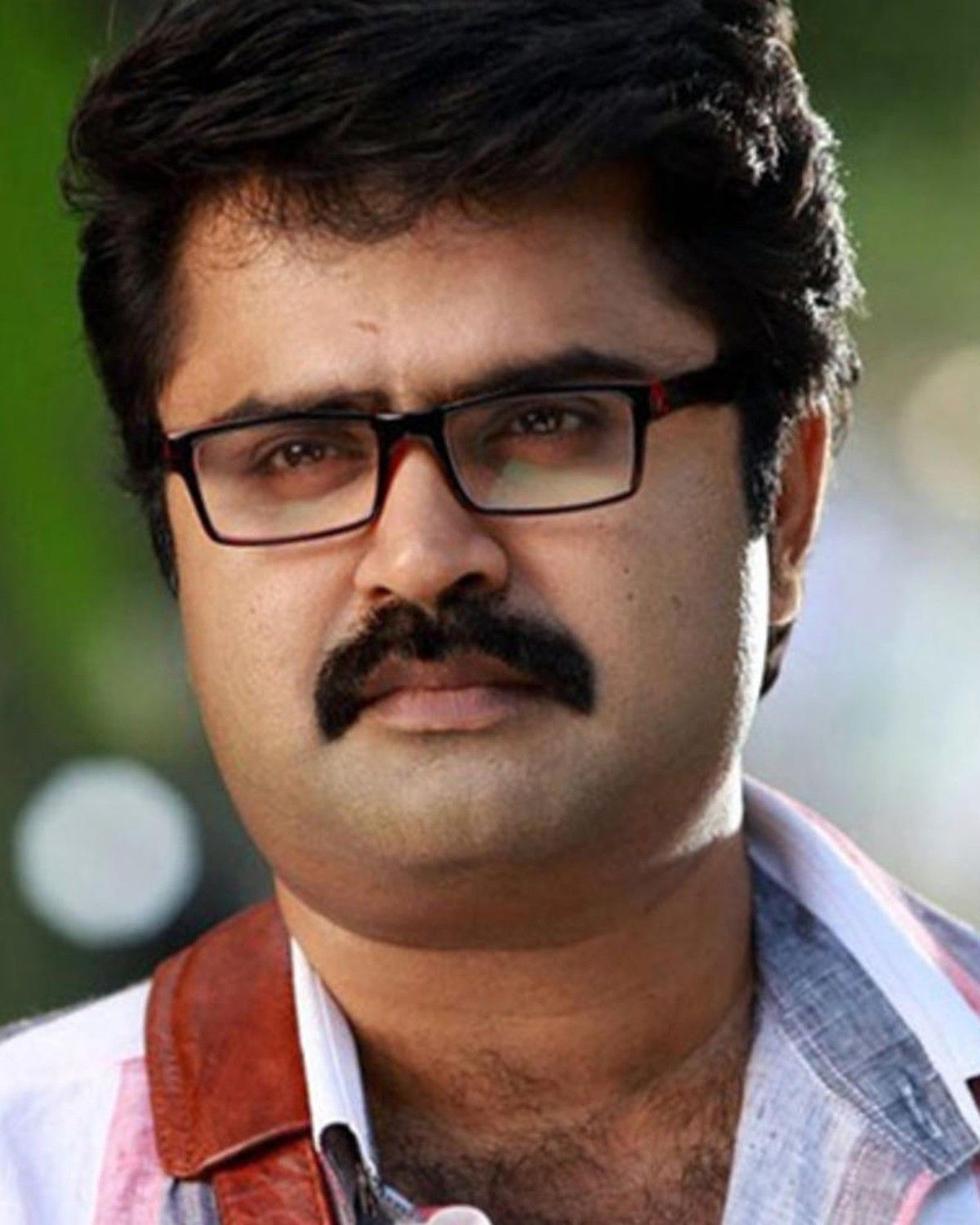 Anoop Menon in glasses with a moustache, close-up outdoor portrait