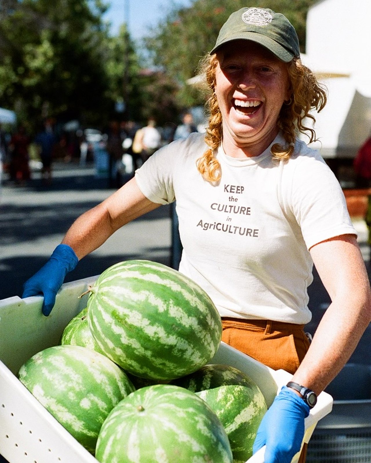 Women holding box of watermelon at farmers market.