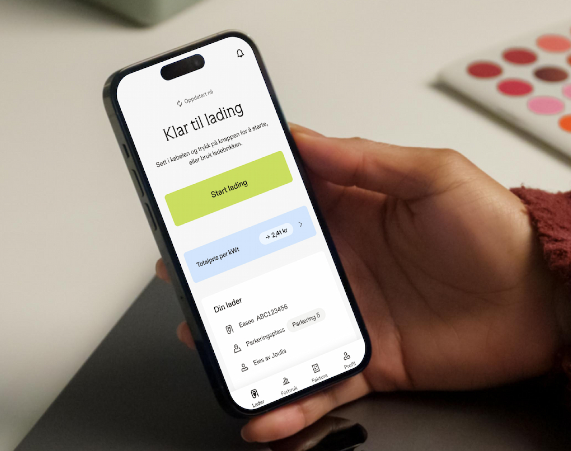 En hånd holder en smarttelefon som viser Joulia ladeapp for elbiler med en «Start lading»-knapp.