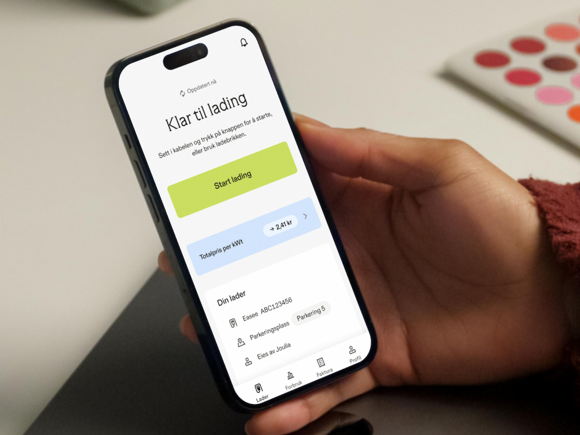 En hånd holder en smarttelefon som viser Joulia ladeapp for elbiler med en «Start lading»-knapp.